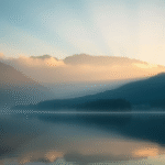 Peaceful mountain landscape with soft morning light filtering through mist, serene lake reflection, calming blue and gold tones, no text no words no letters