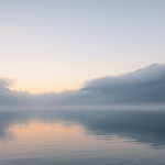 Serene mountain lake at dawn with soft mist, peaceful atmosphere, calm waters reflecting sky, tranquil landscape, no text no words no letters