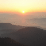 Peaceful sunrise over calm misty mountains with soft golden light creating serene atmosphere no text no words no letters