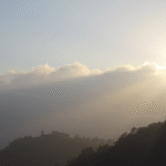Serene mountain landscape with misty clouds clearing to reveal sunlight, peaceful morning atmosphere, soft natural lighting, no text no words no letters