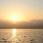 Serene sunrise over calm lake with misty mountains, soft golden light reflecting on water, peaceful nature scene, no text no words no letters