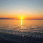 Peaceful sunrise over calm lake with soft golden light reflecting on water creating serene atmosphere for mental clarity no text no words no letters