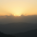 Peaceful mountain sunrise with soft golden light filtering through misty clouds creating sense of hope and tranquility no text no words no letters