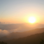 Peaceful sunrise over calm mountain landscape with misty clouds, soft golden light, serene atmosphere, mental clarity concept, no text no words no letters