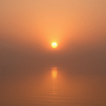 Peaceful sunrise breaking through morning mist over calm water, soft golden light, serenity and hope, no text no words no letters
