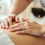 Close-up of massage therapist's hands working on client's shoulder with serene expression, natural lighting, calm spa environment, photorealistic professional healthcare setting