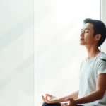 Person in peaceful meditation pose sitting by a window with soft natural light streaming in, eyes closed in calm focus, serene expression, minimalist background with plants