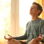 A parent sitting peacefully in a sunlit room, eyes closed in meditation, with soft golden light streaming through windows, representing mental wellness and stress relief through mindfulness practices
