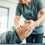 Licensed physical therapist performing hands-on manual therapy on patient's knee, bright clinical setting, professional medical environment, natural lighting