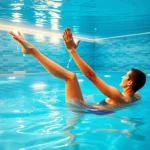 Person doing physical therapy exercises in warm therapeutic pool with underwater lighting, professional aquatic therapy facility, clear water showing legs and arms in motion
