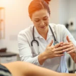 Physical therapist performing hands-on manual therapy assessment on patient's shoulder, clinical rehabilitation setting, professional medical environment, warm lighting, focused clinical care